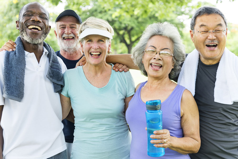 A diverse group of five happy senior residents laughing together outside the property
